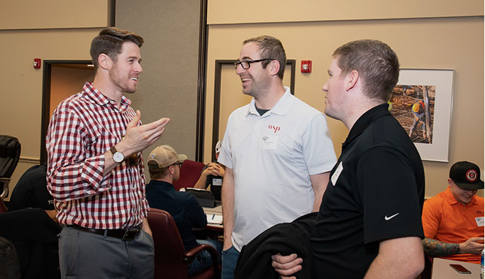 Three men at a CoP event smile while talking together at an event.